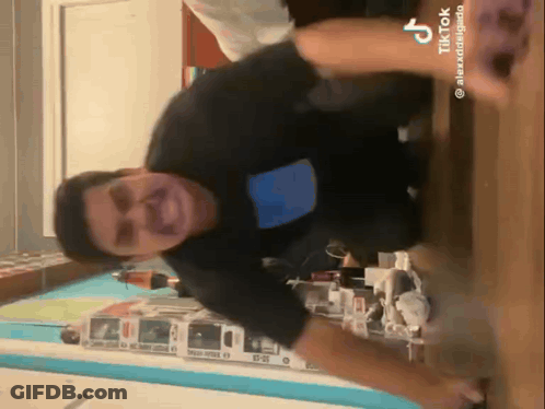 A Man In A Black Shirt Is Standing On A Wooden Floor In A Room With A Blue Wall . GIF