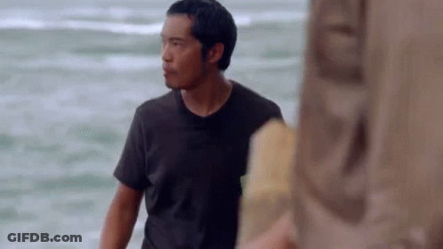 A Man In A Black Shirt Is Standing On The Beach Looking At The Ocean . GIF
