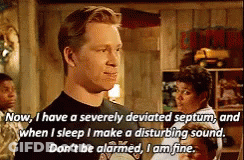 A Man In A Black Shirt Is Talking About A Disturbing Sound While Standing In A Room . GIF