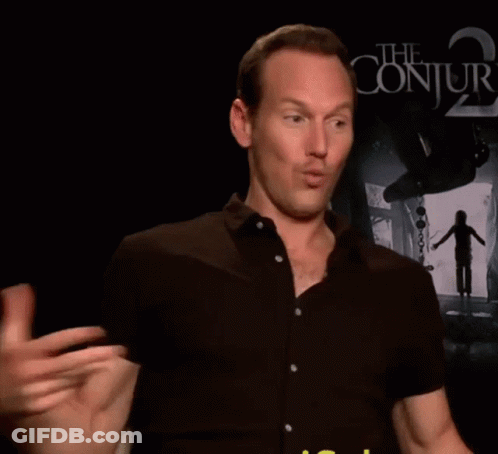 A Man In A Black Shirt Is Talking In Front Of A Poster For The Conjuring 2 GIF