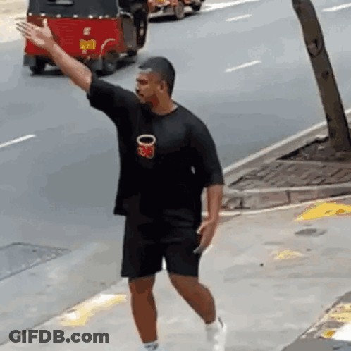 A Man In A Black Shirt Is Walking Down A Sidewalk While A Red Rickshaw Is Driving Behind Him . GIF