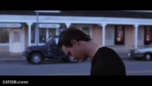 A Man In A Black Shirt Is Walking Down A Street . GIF