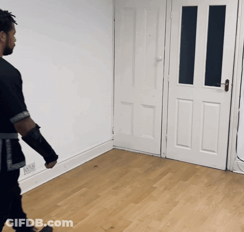 A Man In A Black Shirt Is Walking In A Room With A White Door GIF