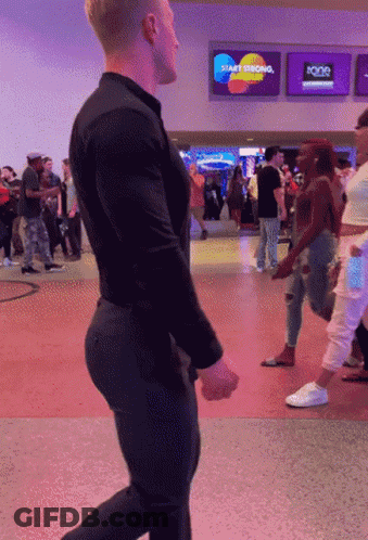 A Man In A Black Shirt Is Walking In Front Of A Sign That Says Start Thinking GIF