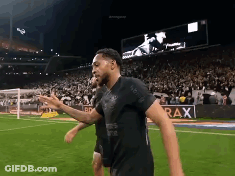 A Man In A Black Shirt Is Walking On A Soccer Field GIF