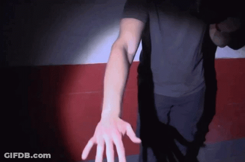 A Man In A Black Shirt Reaches Out His Hand Towards The Camera GIF