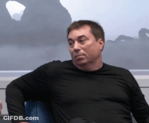 A Man In A Black Shirt Sits In A Chair GIF