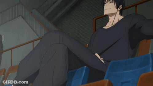 A Man In A Black Shirt Sits In A Stadium With His Legs Crossed GIF