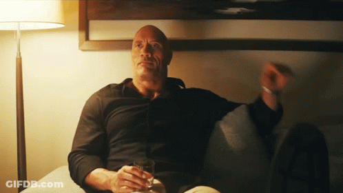 A Man In A Black Shirt Sits On A Couch Holding A Glass Of Whiskey GIF