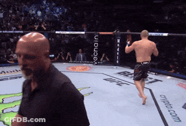 A Man In A Black Shirt Stands In A Boxing Ring With The Word Ufc On The Ground GIF