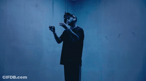 A Man In A Black Shirt Stands In A Dark Room GIF