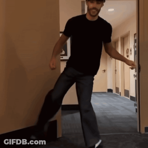 A Man In A Black Shirt Stands In A Hallway GIF