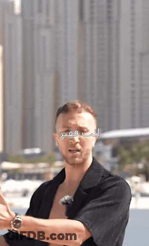 A Man In A Black Shirt Stands In Front Of A City Skyline With Arabic Writing On It GIF