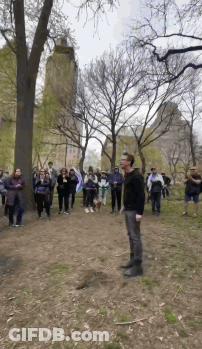 A Man In A Black Shirt Stands In Front Of A Crowd In A Park GIF