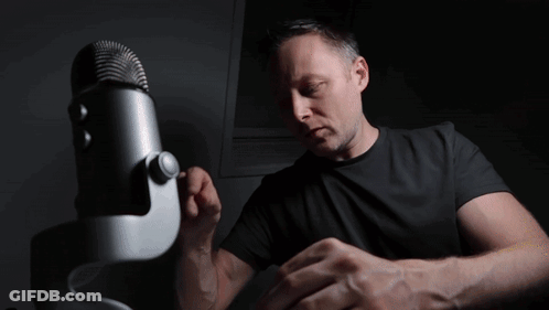 A Man In A Black Shirt Stands In Front Of A Microphone With A Bbc Logo In The Background GIF
