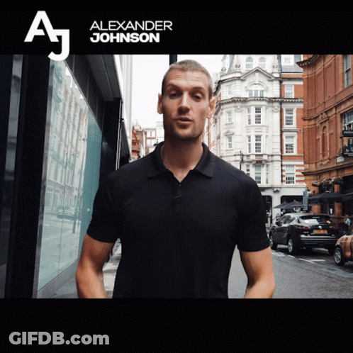 A Man In A Black Shirt Stands In Front Of A Sign That Says " Alexander Johnson " GIF