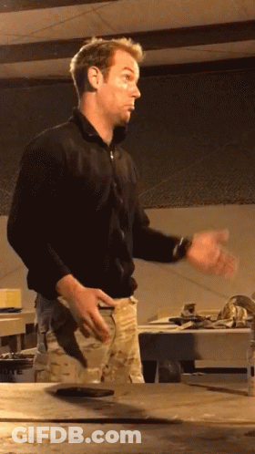 A Man In A Black Shirt Stands In Front Of A Table With His Hands Outstretched GIF