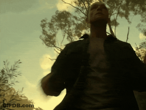 A Man In A Black Shirt Stands In Front Of A Tree GIF
