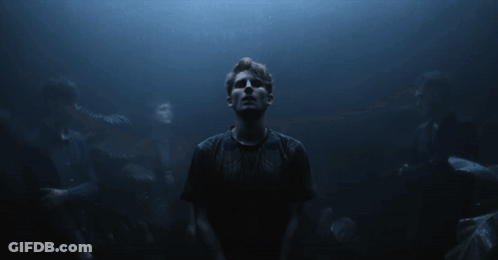 A Man In A Black Shirt Stands In The Dark GIF