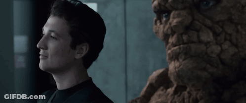 A Man In A Black Shirt Stands Next To A Statue Of A Face GIF