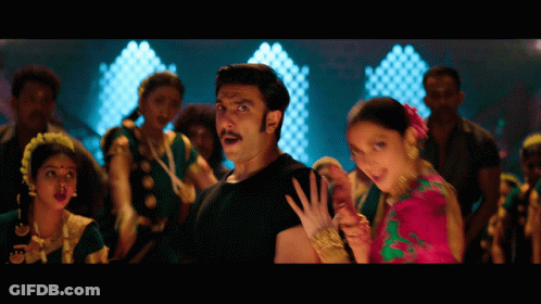 A Man In A Black Shirt Stands Next To A Woman In A Pink And Green Dress GIF