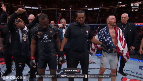 A Man In A Black Shirt That Says Ufc Stands Next To A Man In An American Flag GIF