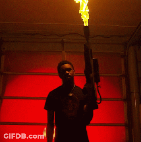 A Man In A Black Shirt With A Skull On It Holds A Flamethrower GIF