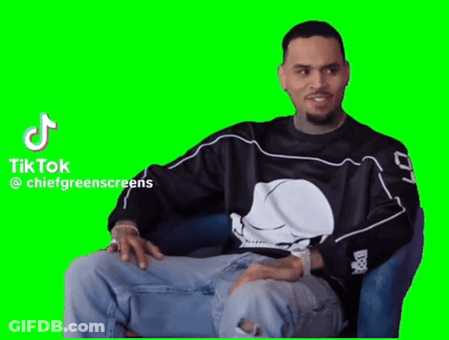 A Man In A Black Shirt With A Skull On It Is Sitting In A Chair On A Green Screen . GIF