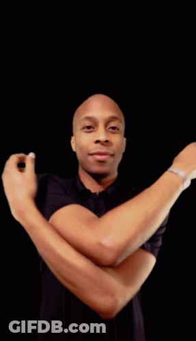 A Man In A Black Shirt With His Arms Crossed Looks At The Camera GIF