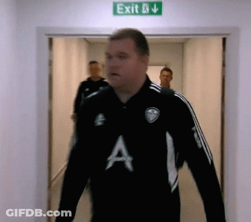 A Man In A Black Shirt With The Letter A On It Walks Through An Exit Sign GIF