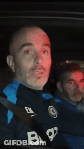 A Man In A Black Shirt With The Letter B On It Is Sitting In A Car . GIF