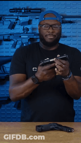 A Man In A Black Shirt With The Letter C On The Front Is Holding A Gun GIF