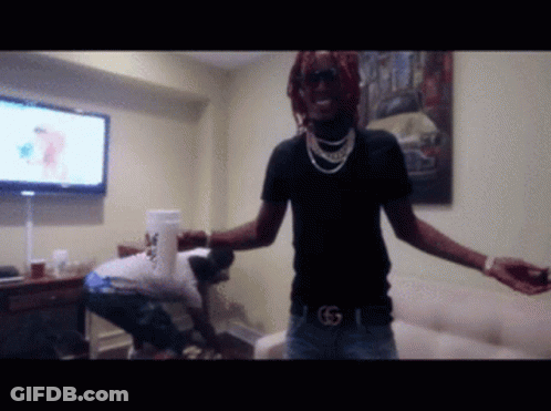 A Man In A Black Shirt With The Letter G On His Belt Stands In A Room GIF