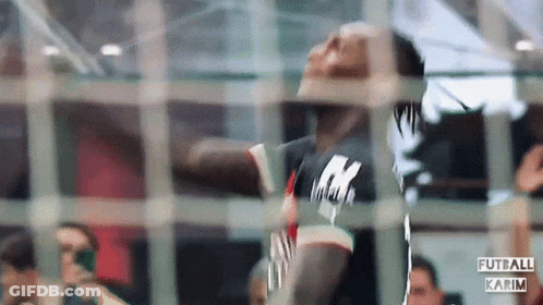 A Man In A Black Shirt With The Letter K On It Is Behind A Fence GIF