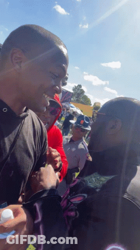 A Man In A Black Shirt With The Letter O On It Talks To Another Man GIF