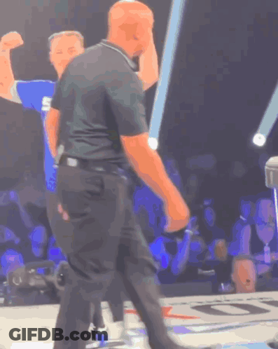 A Man In A Black Shirt With The Letter S On It Stands In Front Of A Crowd GIF