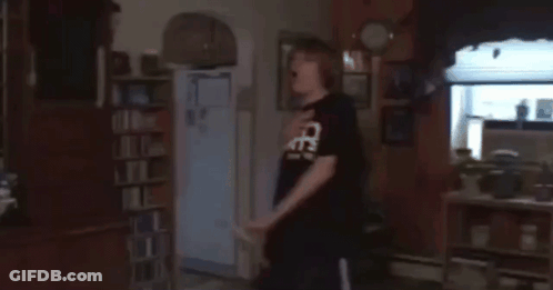 A Man In A Black Shirt With The Word Cats On It Is Standing In A Living Room GIF