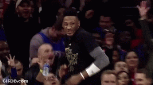 A Man In A Black Shirt With The Word Victory On It Is Standing In Front Of A Crowd Of People . GIF