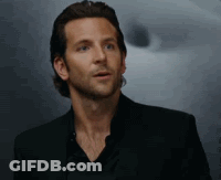 A Man In A Black Suit And Black Shirt Is Standing In Front Of A Wall . GIF