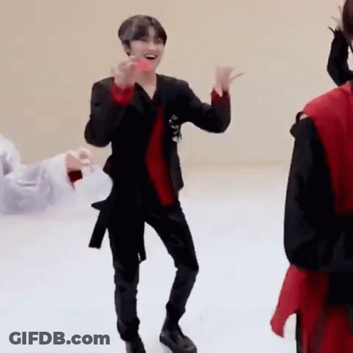 A Man In A Black Suit And Red Shirt Is Dancing On A White Floor While Holding A Donut . GIF