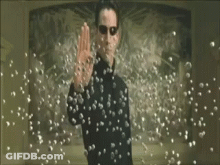 A Man In A Black Suit And Sunglasses Is Standing In Front Of A Bunch Of Bullets . GIF