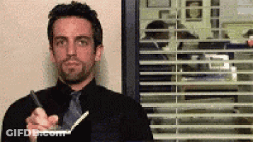 A Man In A Black Suit And Tie Is Holding A Pen And A Notebook GIF
