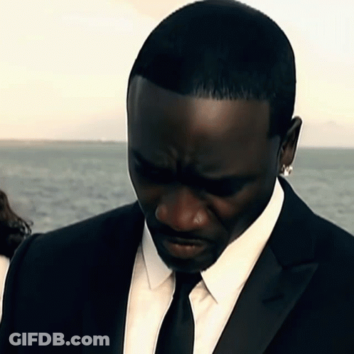 A Man In A Black Suit And Tie Looks Down GIF