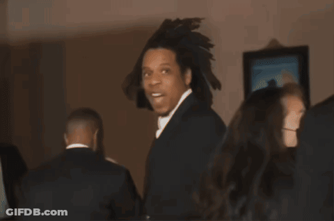 A Man In A Black Suit And White Tie Is Standing In A Room GIF