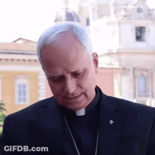 A Man In A Black Suit Has A Badge On His Lapel That Says ' Cardinal ' On It GIF