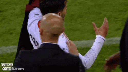 A Man In A Black Suit Holds A Soccer Player In A White Jersey That Says Karim GIF
