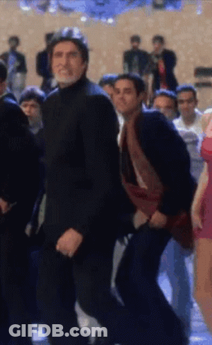 A Man In A Black Suit Is Dancing In A Crowd Of People GIF