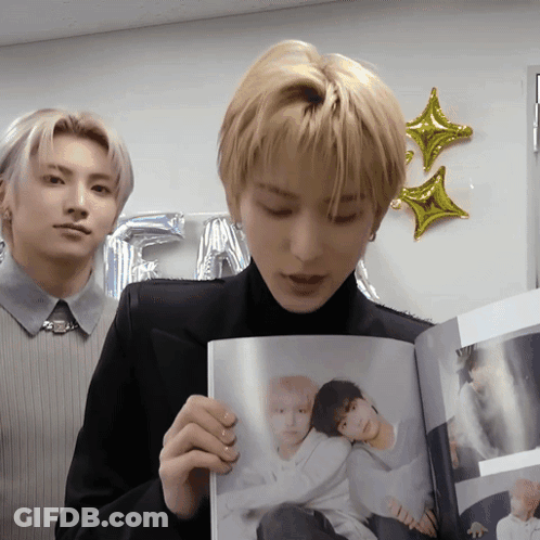 A Man In A Black Suit Is Holding A Book With A Picture Of Two People On It GIF