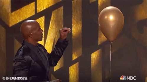 A Man In A Black Suit Is Holding A Gold Balloon In Front Of A Nbc Logo GIF