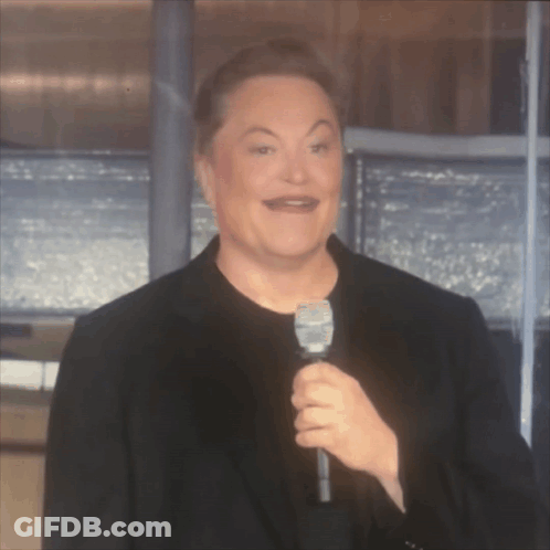 A Man In A Black Suit Is Holding A Microphone And Making A Funny Face GIF